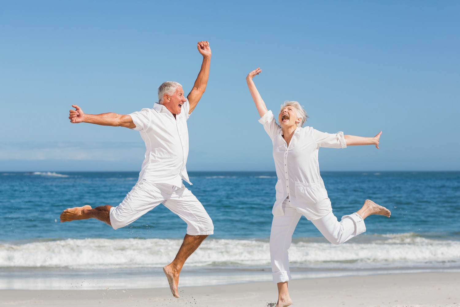 Senior couple jumping at the beach on a sunny day
